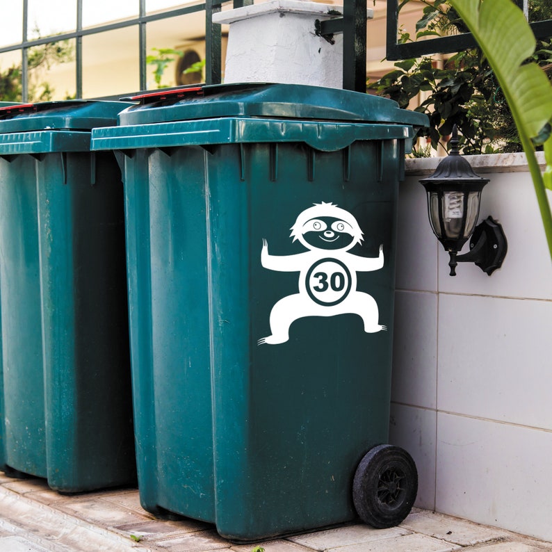 May include: Two green recycling bins with wheels. The bin on the right has a white sloth sticker with a 30 km/h speed limit sign.