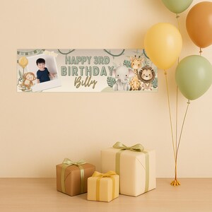 Puede incluir: Una pancarta de cumplea&ntilde;os con el texto "HAPPY 3RD BIRTHDAY Billy" e ilustraciones de animales de la jungla. La pancarta est&aacute; decorada con una foto de un ni&ntilde;o y un mono. Varios globos en tonos amarillos y verdes flotan sobre los regalos.