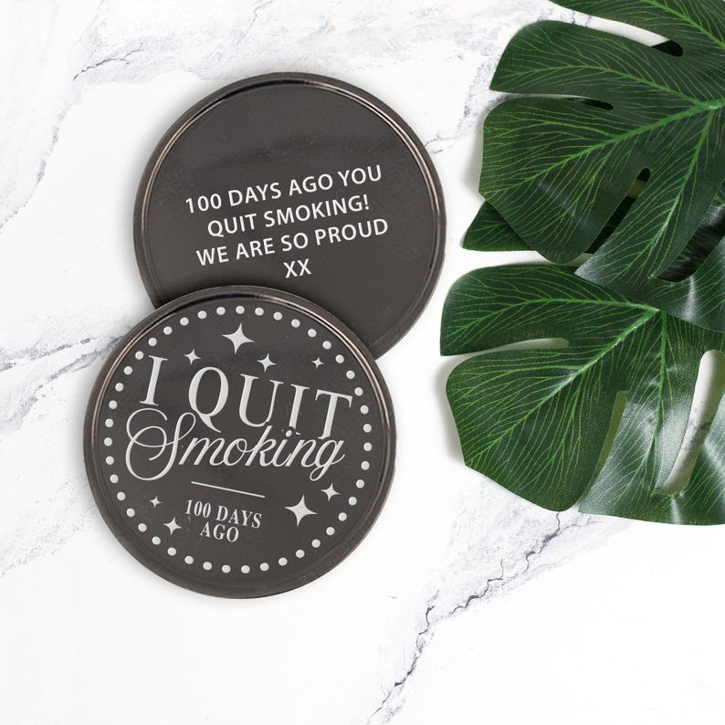 May include: Two black round coasters with silver trim. One coaster reads "I QUIT Smoking 100 DAYS AGO" with star accents. The other coaster reads "100 DAYS AGO YOU QUIT SMOKING! WE ARE SO PROUD XX".