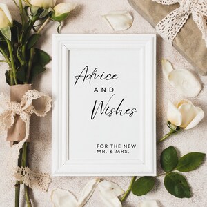 May include: White frame with a sign that says "Advice and Wishes for the New Mr. & Mrs."  The frame is surrounded by white roses and petals.