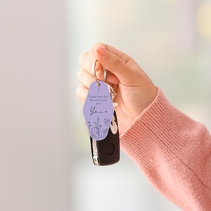 Puede incluir: Un llavero lila con un llavero plateado y una llave de coche. El llavero tiene el texto "If mums were like flowers, I would pick You" con ilustraciones florales. El llavero est&aacute; sujeto por una persona.