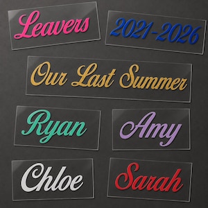 May include: A collection of clear acrylic name tags with colorful text. The tags feature names like "Ryan," "Amy," "Chloe," and "Sarah," along with phrases such as "Leavers," "2021-2026," and "Our Last Summer."