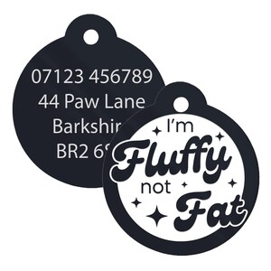 May include: Black and white round pet ID tag with the text "I'm Fluffy not Fat" in a stylized font. The tag also has a black circle with white text that includes a phone number, address, and postcode.