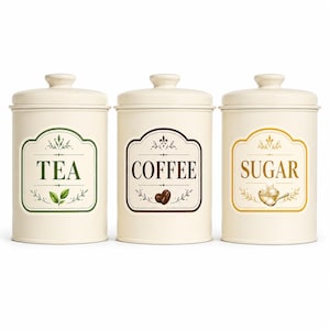May include: A set of three cream-colored cylindrical canisters with matching lids. Each canister features a decorative label with text and illustrations: one labeled TEA with green leaves, one COFFEE with beans, and one SUGAR with sugar cubes.