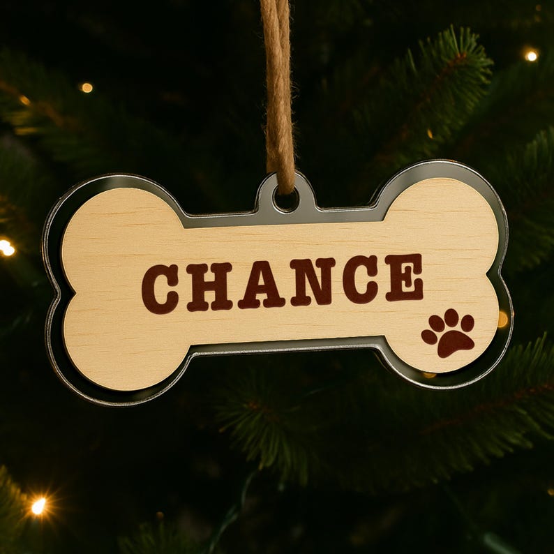 Peut inclure: Ornement en forme d'os pour chien avec le nom "CHANCE" en lettres marron. L'ornement a un centre en grain de bois clair, un bord argent&eacute; et une empreinte de patte. Une ficelle marron est attach&eacute;e pour l'accrocher.