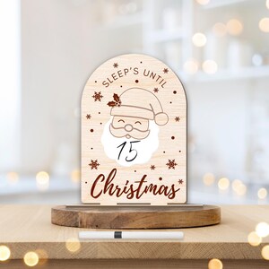 May include: Wooden countdown sign featuring a Santa Claus illustration and the text "Sleep's Until Christmas". The sign has a white dry-erase surface for writing the number of days until Christmas.