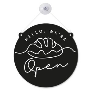 以下が含まれることがあります： 「HELLO, WE'RE Open」の白い文字とパンの線画が描かれた丸い黒い看板。白いコードと吸盤で吊り下げられています。パン屋やカフェに最適です。