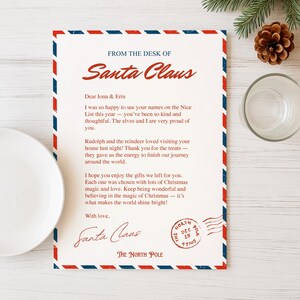 May include: A letter from Santa Claus with a red, white, and blue border. The letter is addressed to Iona & Erin and includes a message about the Nice List, Rudolph, and Christmas gifts. A pine cone and glass are in the background.