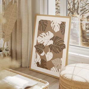 May include: A framed print with a brown background and white and brown stylized monstera leaves. The print is in a wooden frame.