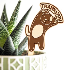 May include: Wooden plant stake with a brown dog holding a sign that says "Thank You".