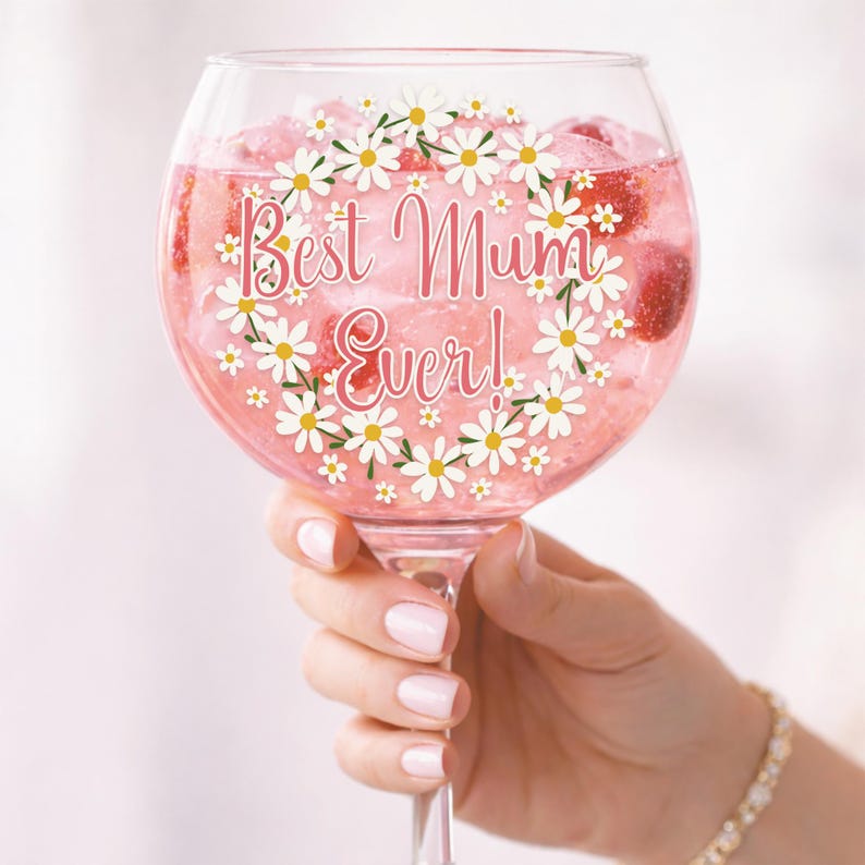 Puede incluir: Una copa grande y transparente llena de una bebida rosa y hielo. La copa est&aacute; decorada con una guirnalda de margaritas y las palabras "Best Mum Ever!". La copa es sostenida por una persona.