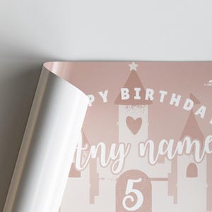 May include: A pink birthday poster with a castle design. The words "Happy Birthday" are arched above the castle, with space for a name and the number "5" below. The poster is partially rolled.