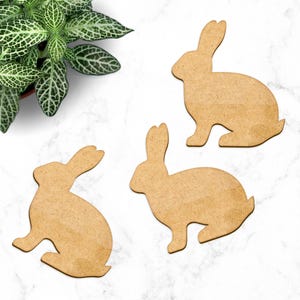 May include: Three wooden rabbit cutouts on a white marble surface. The rabbits are all facing the same direction and are in a sitting position.