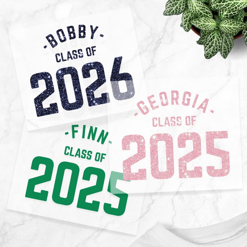 May include: Three white squares with text for graduation announcements. The top square reads "-BOBBY- CLASS OF 2026" in navy blue glitter. The middle square reads "-FINN- CLASS OF 2025" in green. The bottom square reads "-GEORGIA- CLASS OF 2025" in pink.