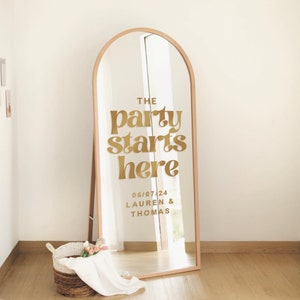 May include: A gold mirror with an arched top and a gold vinyl sticker that says "The party starts here 06/07/24 Lauren & Thomas"