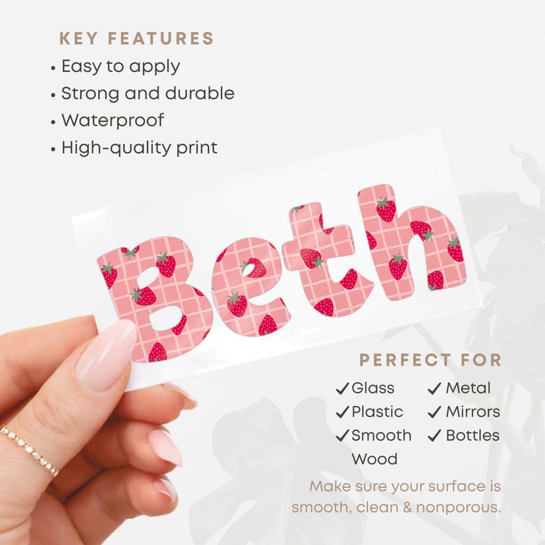 May include: A white sticker with the name "Beth" in pink letters, each decorated with red strawberries. The sticker is held by a hand with a gold ring. The sticker is perfect for glass, metal, plastic, mirrors, smooth surfaces, and bottles.