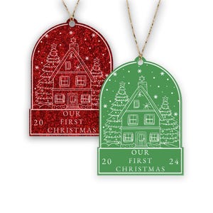 May include: Two Christmas ornaments, one red and one green, with a white outline of a house, trees, and the text "Our First Christmas" and the years "20" and "24".