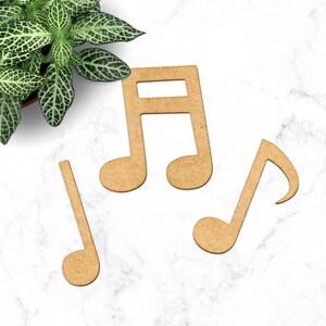 May include: Three wooden music note shapes, two are treble clefs and one is a bass clef. The notes are light brown and are on a white marble surface.