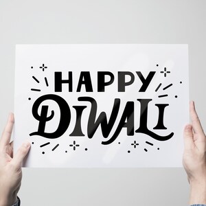May include: A white sign with black text that reads "Happy Diwali" with a stylised design of fireworks around the text.