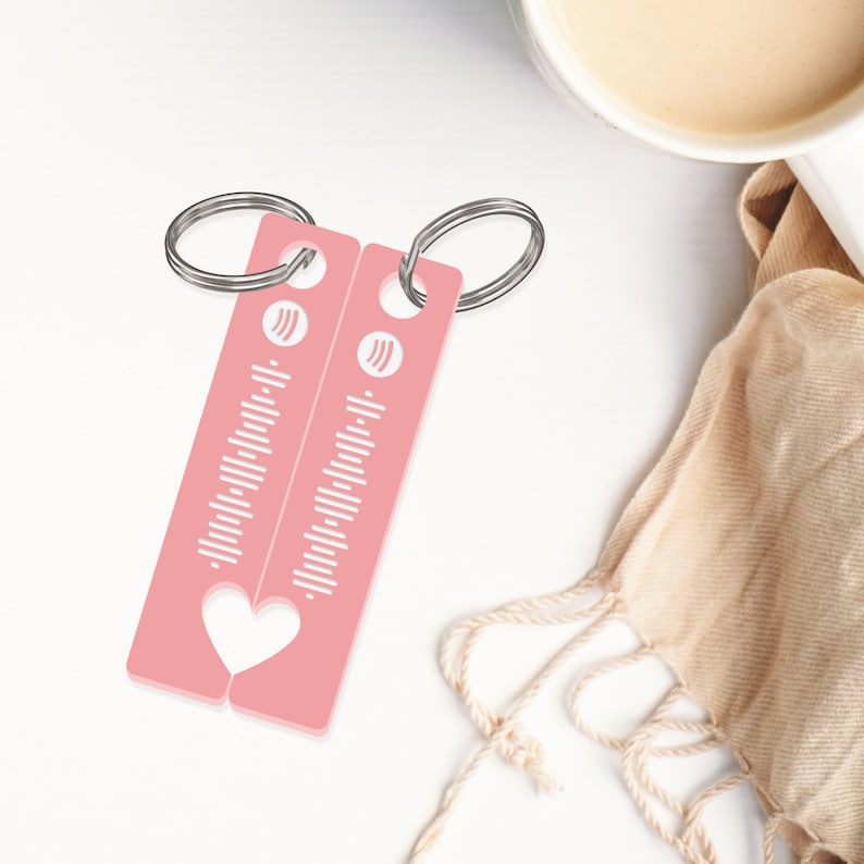 May include: Two pink keychains with a heart cut out in the middle. Each keychain has a white musical note symbol and a series of white lines that resemble a music equalizer.