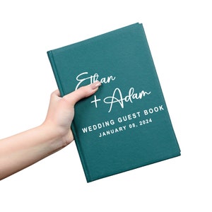 May include: A teal green hardcover wedding guest book with the names "Ethan + Adam" and the date "January 08, 2024" printed in white.