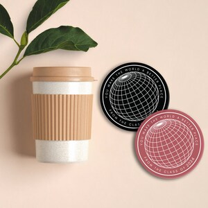 May include: Two black and white round coasters with the text "You make the world a better place from the class of 2024" and a graphic of a globe. One coaster has a black globe and the other has a pink globe.