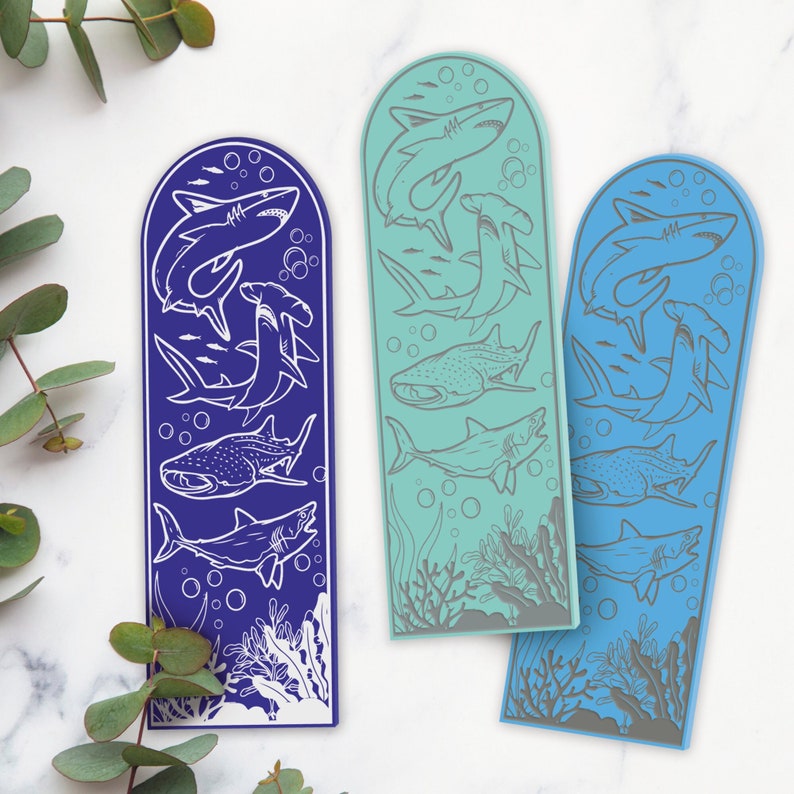 May include: Three blue and purple bookmarks with a white outline of various sharks and fish. The bookmarks are shaped like a fin and have a white outline of a shark on the top.