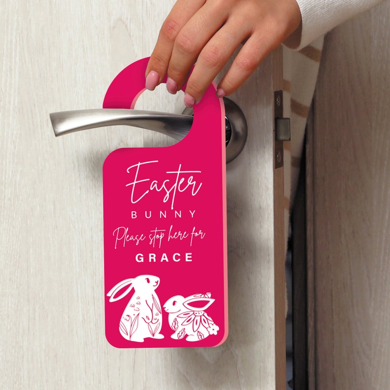 May include: Pink door hanger with the text "Easter Bunny" and "Please stop here for GRACE". Two white bunny illustrations are at the bottom of the hanger.