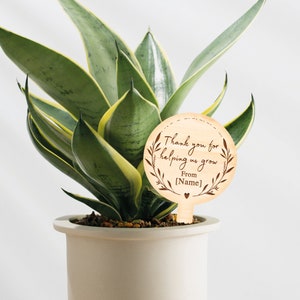 May include: Wooden plant stake with the text "Thank you for helping us grow. From [Name]" with a heart symbol.