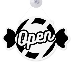 May include: A white and black candy-shaped sign with the word "Open" in a cursive font. The sign is hanging from a suction cup. The design features black stripes and black candy wrapper ends.