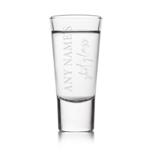 May include: A clear shot glass with the text "ANY NAME'S shot glass" etched on the front. The glass is filled with a clear liquid. The shot glass has a thick base and a straight, cylindrical body.