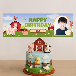 May include: A farm-themed birthday cake with a blue sky design, featuring a red barn, pig, cow, sheep, and chick figurines. The cake is decorated with a fence and green grass. A banner above says "Happy Birthday Ben".