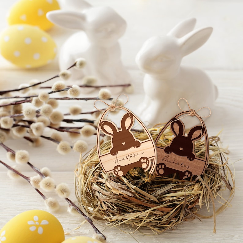 May include: Two wooden Easter egg ornaments with bunny cutouts and personalized names "Anastasia" and "Nicholas". The ornaments are nestled in a straw nest.