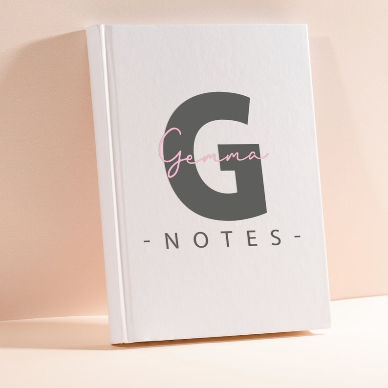 Pode incluir: Caderno branco com uma grande letra G cinza e a palavra "Gemma" escrita em it&aacute;lico rosa acima. O texto "NOTES" est&aacute; escrito em preto abaixo da letra G.