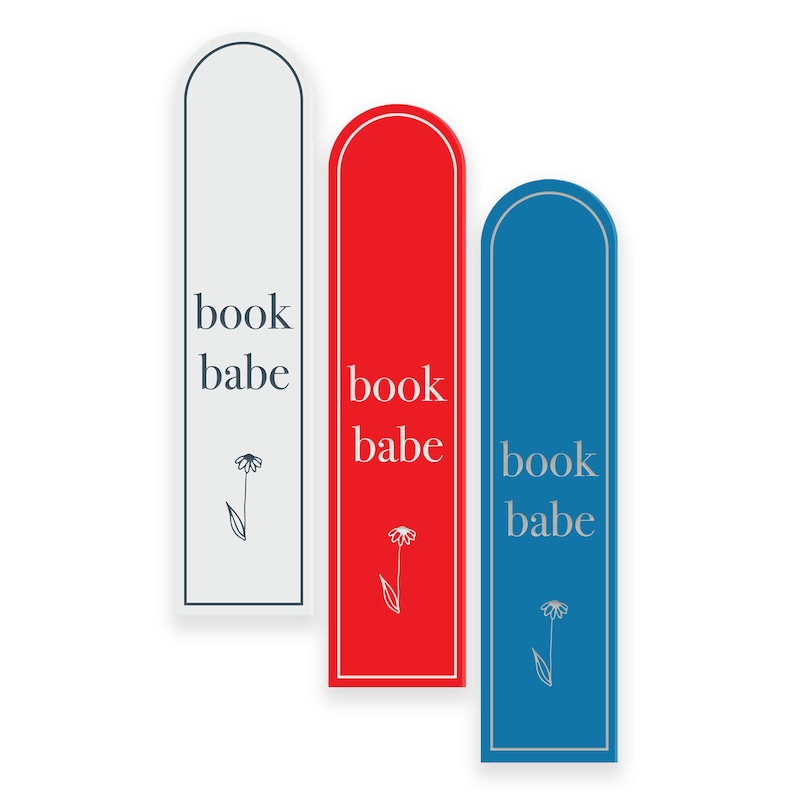 May include: Three bookmarks with rounded edges and a simple floral design. Each bookmark is a different color: white, red, and blue. The text "book babe" is printed on each bookmark.