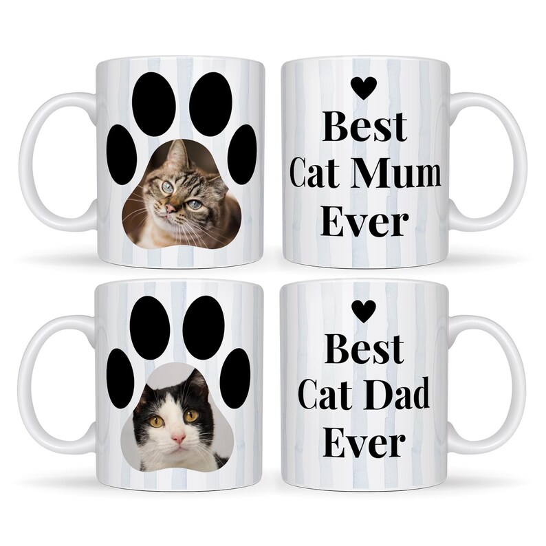 May include: Four white ceramic mugs with cat-themed designs. Two mugs feature a cat paw print with a cat's face inside. The other two mugs have the text "Best Cat Mum Ever" and "Best Cat Dad Ever" with a heart symbol. The mugs have a blue striped background.