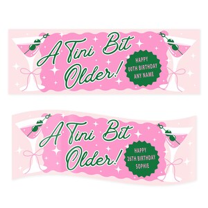 Op de afbeelding: Roze verjaardagsbanner met de tekst "A Tini Bit Older!" in groen schrift. De banner toont martiniglazen, sterren en een groene cirkel met "Happy 00th Birthday Any Name" of "Happy 26th Birthday Sophie".