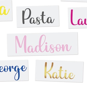 May include: Rectangular white stickers with various words and names in different colors. The word "Pasta" is in dark gray, "Madison" in pink, "Katie" in gold, and "George" in blue. The stickers are arranged on a white background.