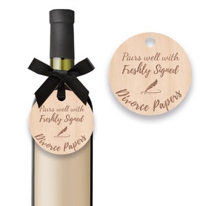K&ouml;nnte beinhalten: Ein Holz-Weinflaschenanh&auml;nger mit dem Text "Pairs well with Freshly Signed Divorce Papers" und einer Federzeichnung. Der Anh&auml;nger ist mit einem schwarzen Band an einer Weinflasche gebunden.