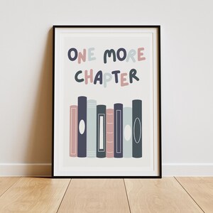 May include: A white framed print with the text "ONE MORE CHAPTER" in pink and blue lettering. The print features a row of colorful books with white circles on the spines.