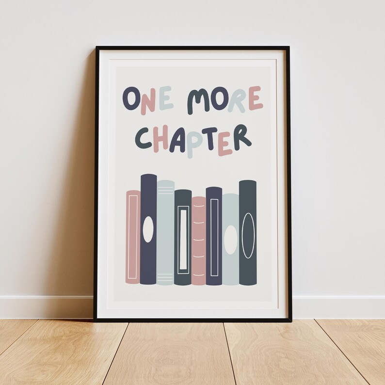 May include: A white framed print with the text "ONE MORE CHAPTER" in pink and blue lettering. The print features a row of colorful books with white circles on the spines.