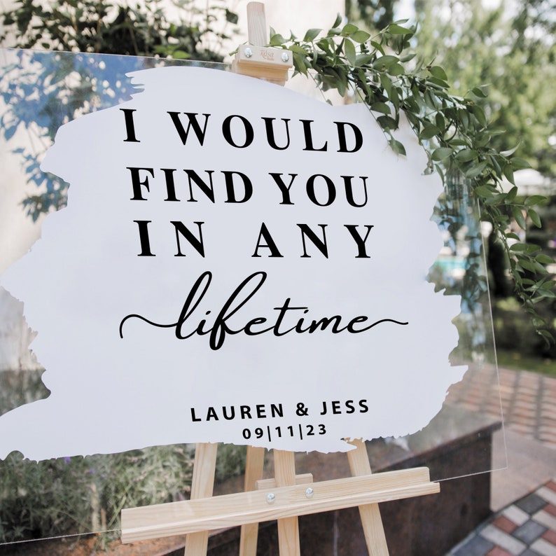 May include: A white acrylic sign with black text on an easel. The text reads "I would find you in any lifetime" with the names "Lauren & Jess" and the date "09/11/23" below.