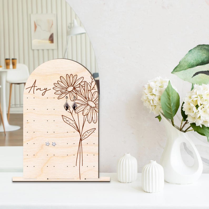 May include: Wooden earring holder with a floral design and the name "Amy" engraved on the front. The holder has multiple holes for earrings.