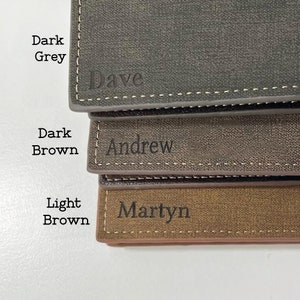 May include: Three personalised leather wallets in dark grey, dark brown, and light brown. The wallets are stacked on top of each other. The top wallet has the name "Dave" engraved on it. The middle wallet has the name "Andrew" engraved on it. The bottom wallet has the name "Martyn" engraved on it.