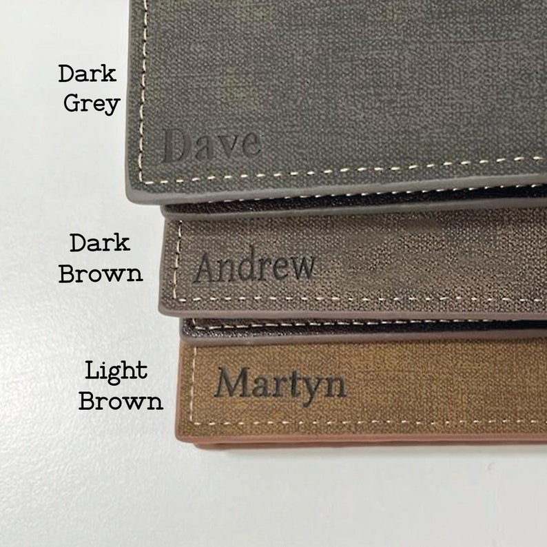 May include: Three personalised leather wallets in dark grey, dark brown, and light brown. The wallets are stacked on top of each other. The top wallet has the name "Dave" engraved on it. The middle wallet has the name "Andrew" engraved on it. The bottom wallet has the name "Martyn" engraved on it.