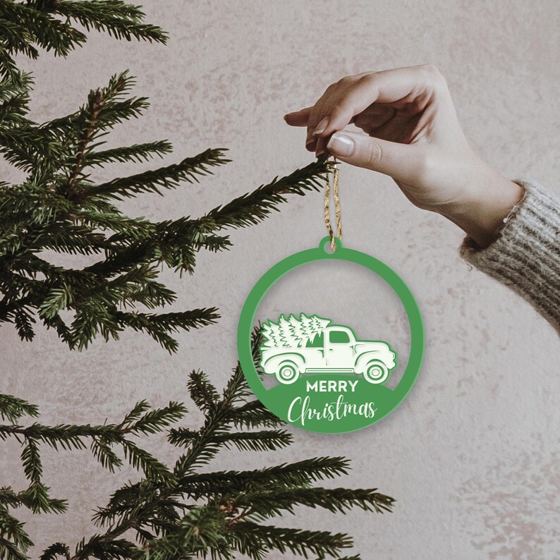 May include: Green circular Christmas ornament with a white silhouette of a truck carrying a Christmas tree and the text "Merry Christmas".