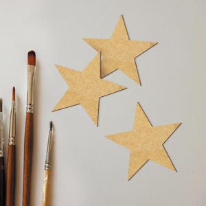 May include: Three brown cardboard stars of different sizes on a white background. Five paintbrushes of different sizes are on the left side of the image.