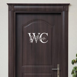 May include: A white vinyl decal with the text "WC Bathroom" on a dark brown wooden door.