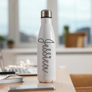 May include: White stainless steel water bottle with a gray cursive name "Jessica" and a small heart on the side.