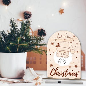 May include: A wooden countdown sign with a Santa Claus illustration and the text "Sleep's Until Christmas". The sign has a white background with brown text and snowflakes. The number "03" is written on the sign.